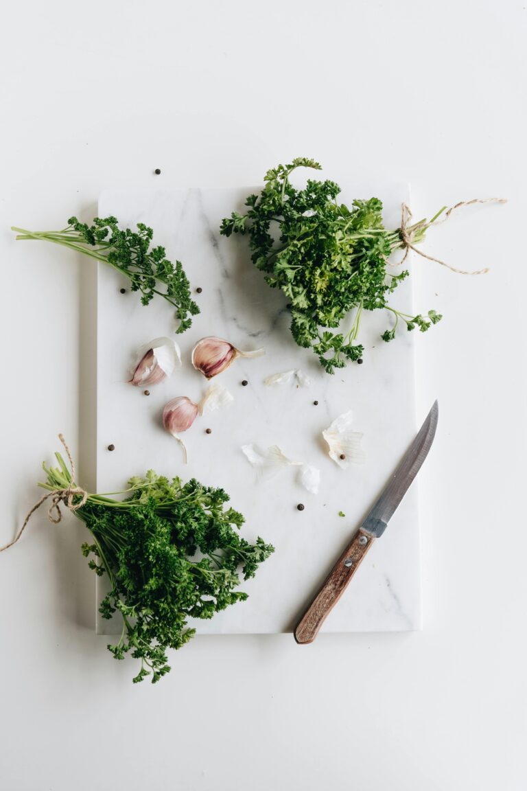 A top-down view of fresh parsley, garlic, and knife on a marble board.